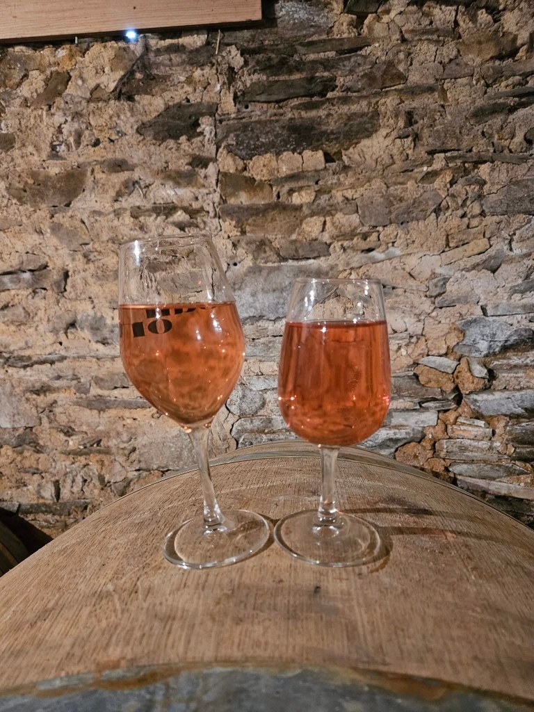 Deux verres de vin posés sur une barrique, devant le mur de pierre de la cave